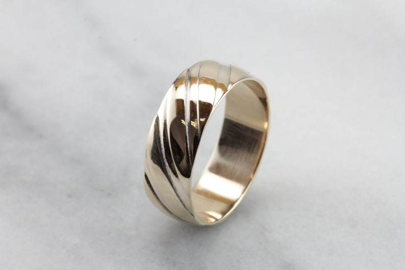 May include: A gold wedding band with a textured, grooved design. The band is polished and has a smooth finish.