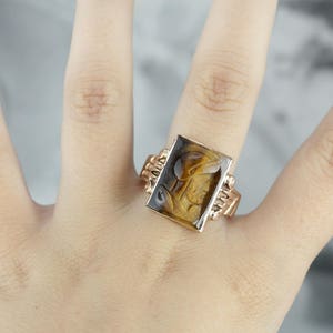 May include: A gold ring with a rectangular brown and black stone set in a gold setting.