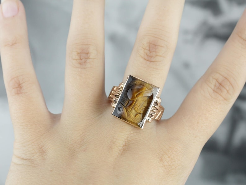 May include: A gold ring with a rectangular brown and black stone set in a gold setting.