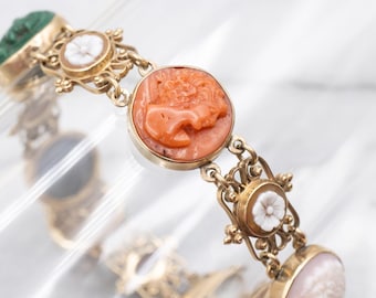 May include: A gold-toned bracelet featuring various cameo designs. The bracelet includes a carved coral cameo, white flower cameos, and a green stone cameo. The bracelet is linked with ornate gold filigree and chain links.