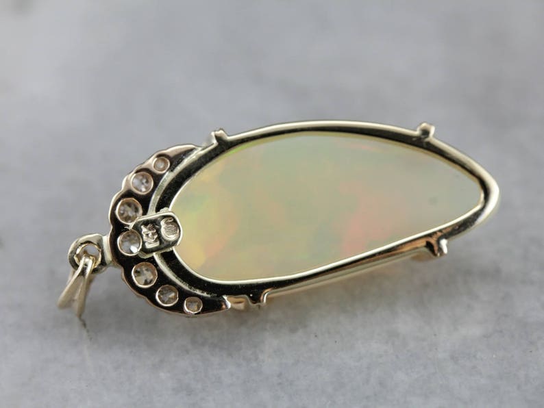 May include: A gold pendant featuring a large oval opal with a delicate halo of small round diamonds. The pendant has a bail for attaching to a chain.