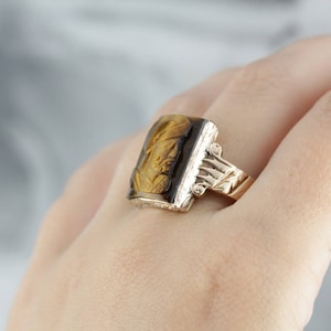 May include: A gold ring with a rectangular tiger's eye stone set in a carved gold band.