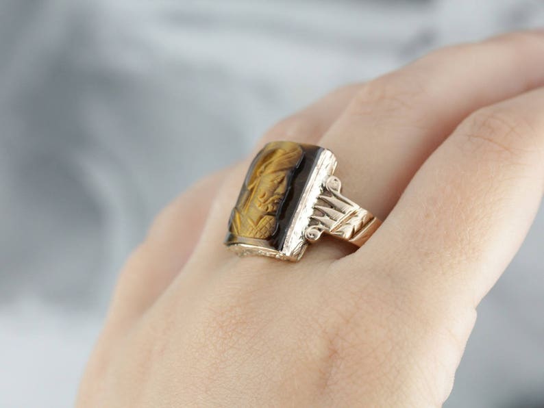 May include: A gold ring with a rectangular tiger's eye stone set in a carved gold band.