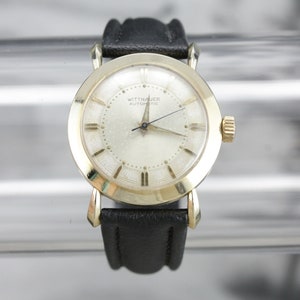 Pu&ograve; includere: Un orologio da polso Wittnauer Automatic color oro con quadrante bianco e cinturino in pelle nera.