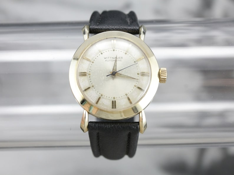 Pu&ograve; includere: Un orologio da polso Wittnauer Automatic color oro con quadrante bianco e cinturino in pelle nera.