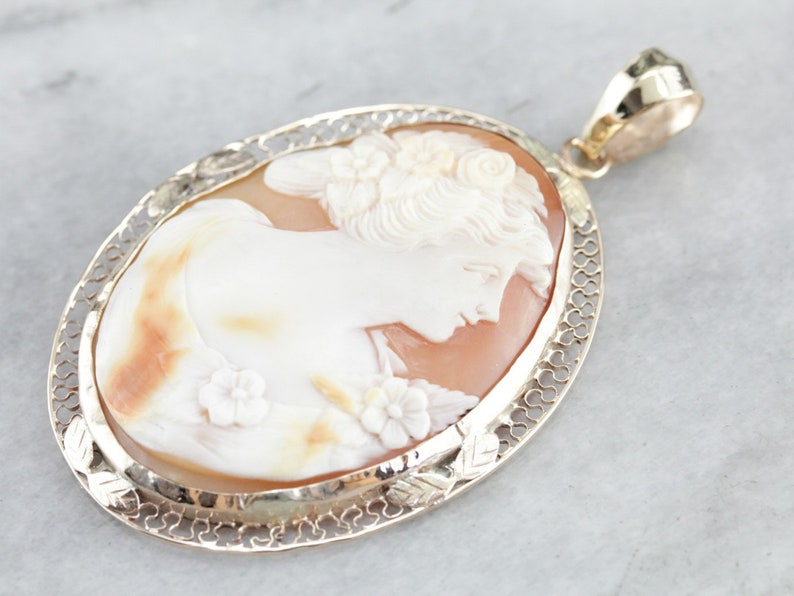 May include: A gold filigree pendant with a cameo of a woman's profile carved from shell. The cameo is set in a delicate gold frame.