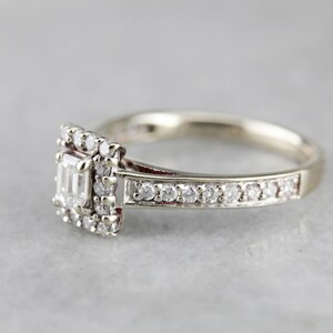 Puede incluir: Un anillo de compromiso de plata con un diamante central de forma cuadrada rodeado de diamantes m&aacute;s peque&ntilde;os. La banda tambi&eacute;n est&aacute; engastada con peque&ntilde;os diamantes.