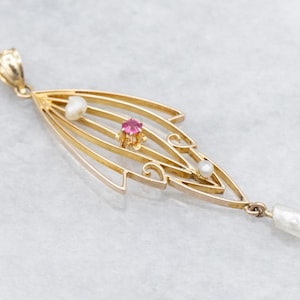 Puede incluir: Colgante de oro con diseño de hoja, con una gema rosa central y tres perlas. El colgante tiene una estructura calada delicada y una perla en forma de pera en la parte inferior. La joya está sobre un fondo claro.