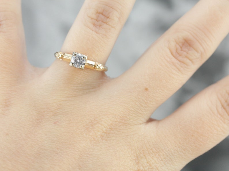 May include: A gold engagement ring with a round, clear diamond set in a simple band. The band is accented with small, round beads.