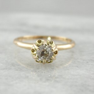Puede incluir: Un delicado anillo de oro con un diamante redondo y transparente engastado en un engaste abierto y detallado.
