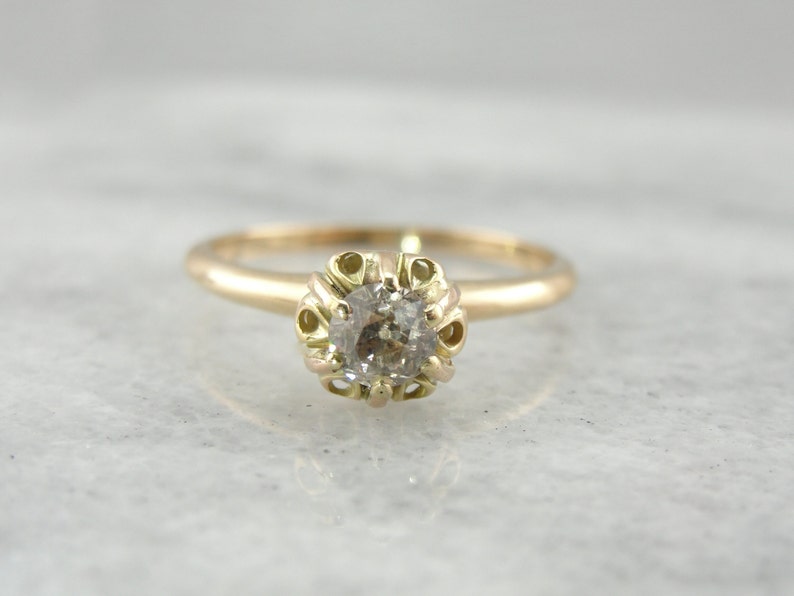 Puede incluir: Un delicado anillo de oro con un diamante redondo y transparente engastado en un engaste abierto y detallado.