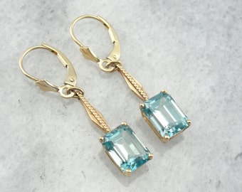 May include: A pair of gold dangle earrings with light blue emerald-cut gemstones. The earrings have a delicate, twisted design.