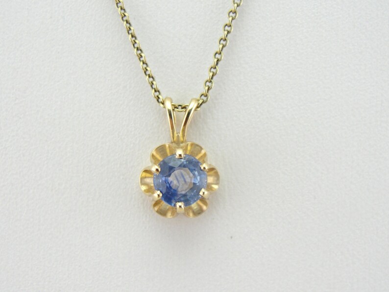 Op de afbeelding: Een delicate gouden ketting met een hanger met een ronde blauwe saffier-steen in een bloemvormig frame.