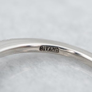 K&ouml;nnte beinhalten: Nahaufnahme eines silbernen Rings mit dem Wort "RITANO" auf dem Band. Der Ring hat eine glatte, polierte Oberfl&auml;che und ein filigranes Design am Rand. Der Hintergrund ist eine weiche, neutrale Farbe.
