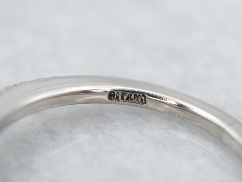 K&ouml;nnte beinhalten: Nahaufnahme eines silbernen Rings mit dem Wort "RITANO" auf dem Band. Der Ring hat eine glatte, polierte Oberfl&auml;che und ein filigranes Design am Rand. Der Hintergrund ist eine weiche, neutrale Farbe.