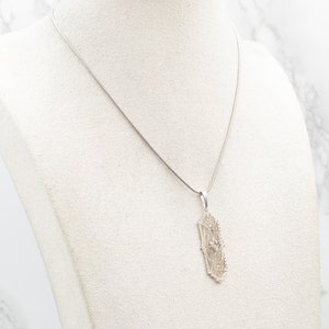 May include: A silver chain necklace with a delicate, intricate pendant. The pendant is shaped like a circle with a geometric design.
