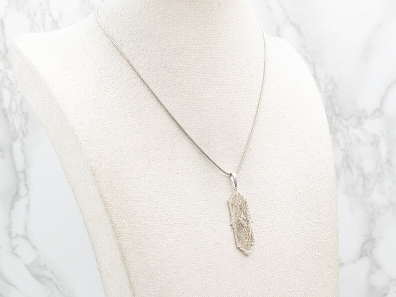 May include: A silver chain necklace with a delicate, intricate pendant. The pendant is shaped like a circle with a geometric design.