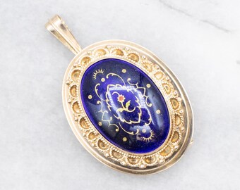 May include: Gold-toned oval pendant with a deep blue enamel center. The enamel is decorated with gold floral and scroll designs. The pendant has a decorative gold border and a loop for a chain. A vintage jewelry piece.