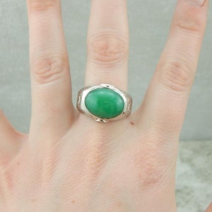 May include: A silver ring with a green oval gemstone set in a textured band.