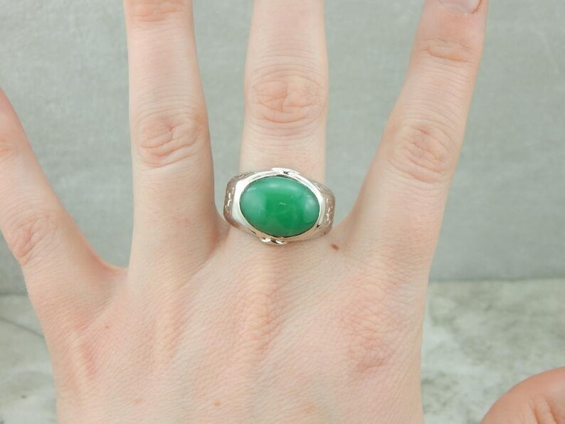 May include: A silver ring with a green oval gemstone set in a textured band.