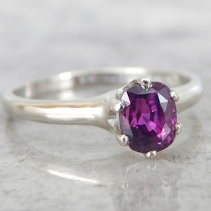 May include: A silver ring with a purple gemstone set in a prong setting.