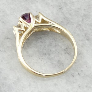 May include: A gold ring with a purple gemstone and two smaller clear gemstones. The ring has a delicate, intricate design.