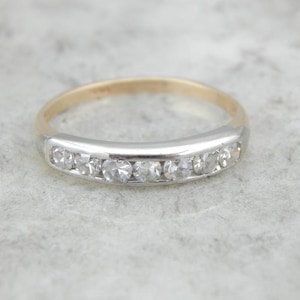 May include: A delicate gold and silver band ring with a row of small, clear gemstones.