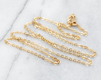 Puede incluir: Un delicado collar de color dorado con un diseño de eslabones circulares repetidos. La cadena está colocada sobre una superficie de mármol blanco y gris. El collar tiene un cierre.