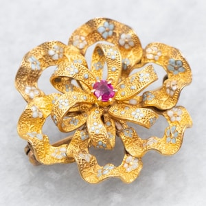 Puede incluir: Un broche de flor de tono dorado con detalles de esmalte blanco y azul. El centro de la flor presenta una piedra preciosa rosa.