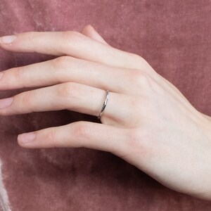 May include: A simple silver band ring worn on a person's finger.