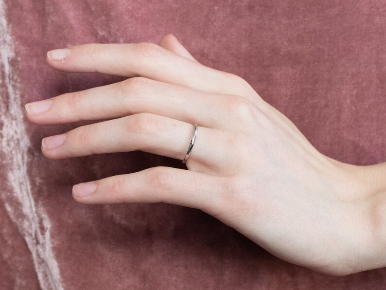 May include: A simple silver band ring worn on a person's finger.