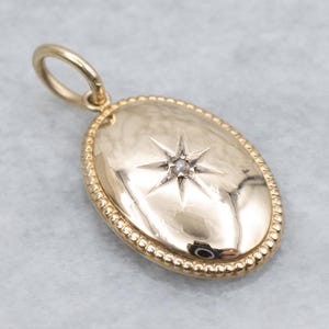 May include: A gold-coloured oval pendant featuring a starburst design with a small gemstone at its centre. The pendant has a beaded border and a loop for a chain. The jewellery piece is likely made of gold.