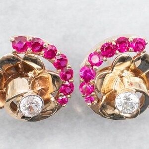 May include: A pair of gold earrings featuring a floral design. The earrings are embellished with a row of pink gemstones and a single diamond at the centre of each flower.