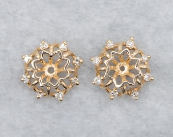 May include: Two gold-toned, star-shaped earrings with a floral design. Each earring features a central open circle surrounded by a star-shaped pattern and small, clear gemstones. The earrings are set against a light gray background.