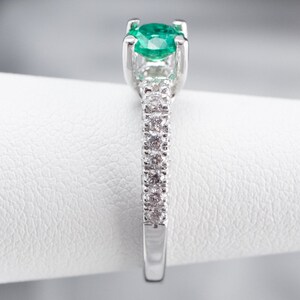 May include: A silver ring featuring a green emerald gemstone and a band of small diamonds.