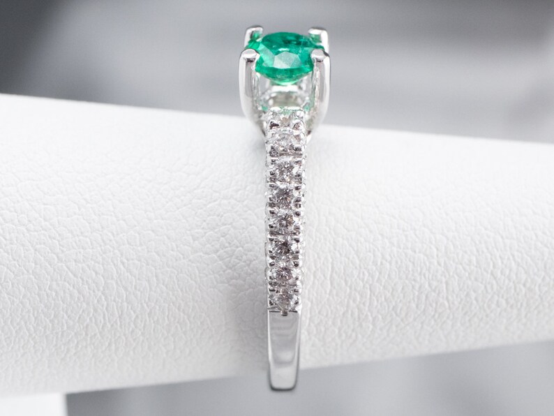 May include: A silver ring featuring a green emerald gemstone and a band of small diamonds.