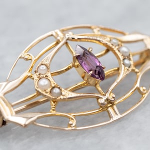 May include: A gold-toned brooch with a delicate, openwork design featuring a purple gemstone and pearl accents.