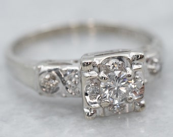 Può includere: Un anello di fidanzamento vintage in oro bianco con un diamante centrale rotondo a taglio brillante e diamanti più piccoli incastonati nella fascia.