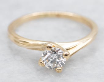 Op de afbeelding: Een gouden verlovingsring met een enkele ronde diamant gezet in een gedraaide band.