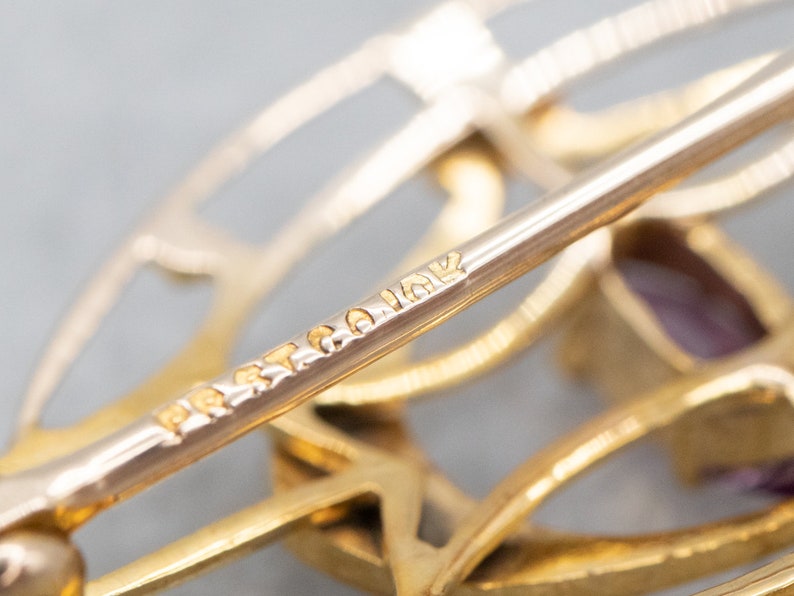 May include: Close-up of a gold-toned brooch with a geometric design. The brooch has a pin on the back and is marked "BRIAR" on the pin.