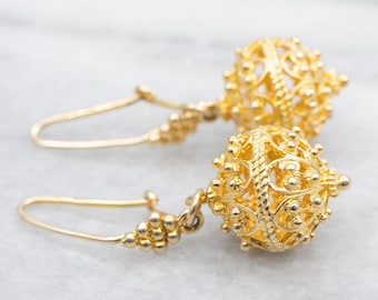 May include: A pair of gold-colored filigree earrings. Each earring features a detailed, openwork sphere design suspended from a hook. The intricate metalwork and overall design suggest a vintage or antique style.