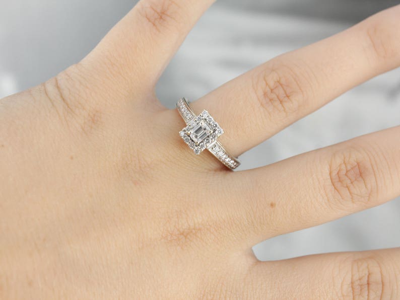 Puede incluir: Un anillo de plata con un diamante talla esmeralda de forma cuadrada rodeado de diamantes m&aacute;s peque&ntilde;os. El anillo tiene una banda que est&aacute; engastada con diamantes m&aacute;s peque&ntilde;os.