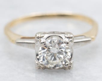 May include: A vintage engagement ring with a large, round, brilliant-cut diamond set in a platinum setting. The ring has a yellow gold band and two smaller diamonds on either side of the center stone.