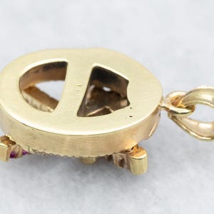 May include: Gold pendant with a peace sign design, featuring red gemstones around the edges. The back of the pendant is smooth and polished.