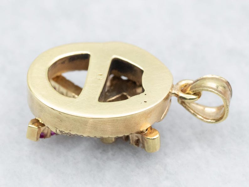May include: Gold pendant with a peace sign design, featuring red gemstones around the edges. The back of the pendant is smooth and polished.