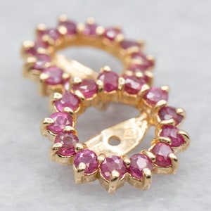 May include: A pair of gold earrings with a circle design. Each earring is set with a row of pink gemstones.