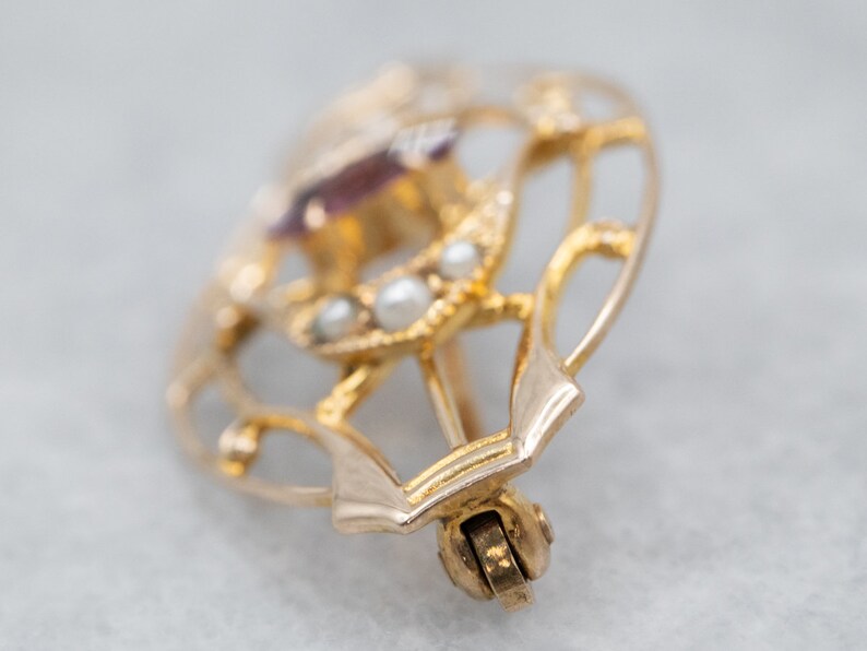May include: A gold heart-shaped brooch with a purple gemstone and pearl accents.