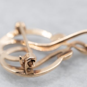 May include: Gold-toned metal brooch with a swirling, abstract design. The brooch has a pin and catch closure.