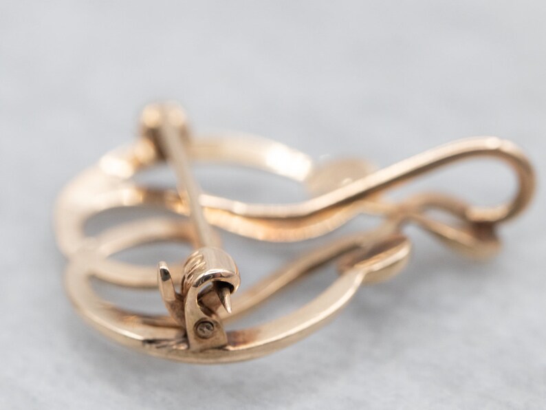 May include: Gold-toned metal brooch with a swirling, abstract design. The brooch has a pin and catch closure.