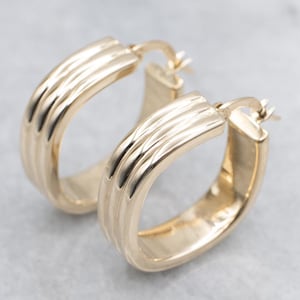 Puede incluir: Un par de pendientes de aro dorados. Cada pendiente tiene forma rectangular con una serie de estrías verticales en la superficie exterior. Los pendientes están hechos de oro amarillo brillante. Miden unos 2,5 cm.